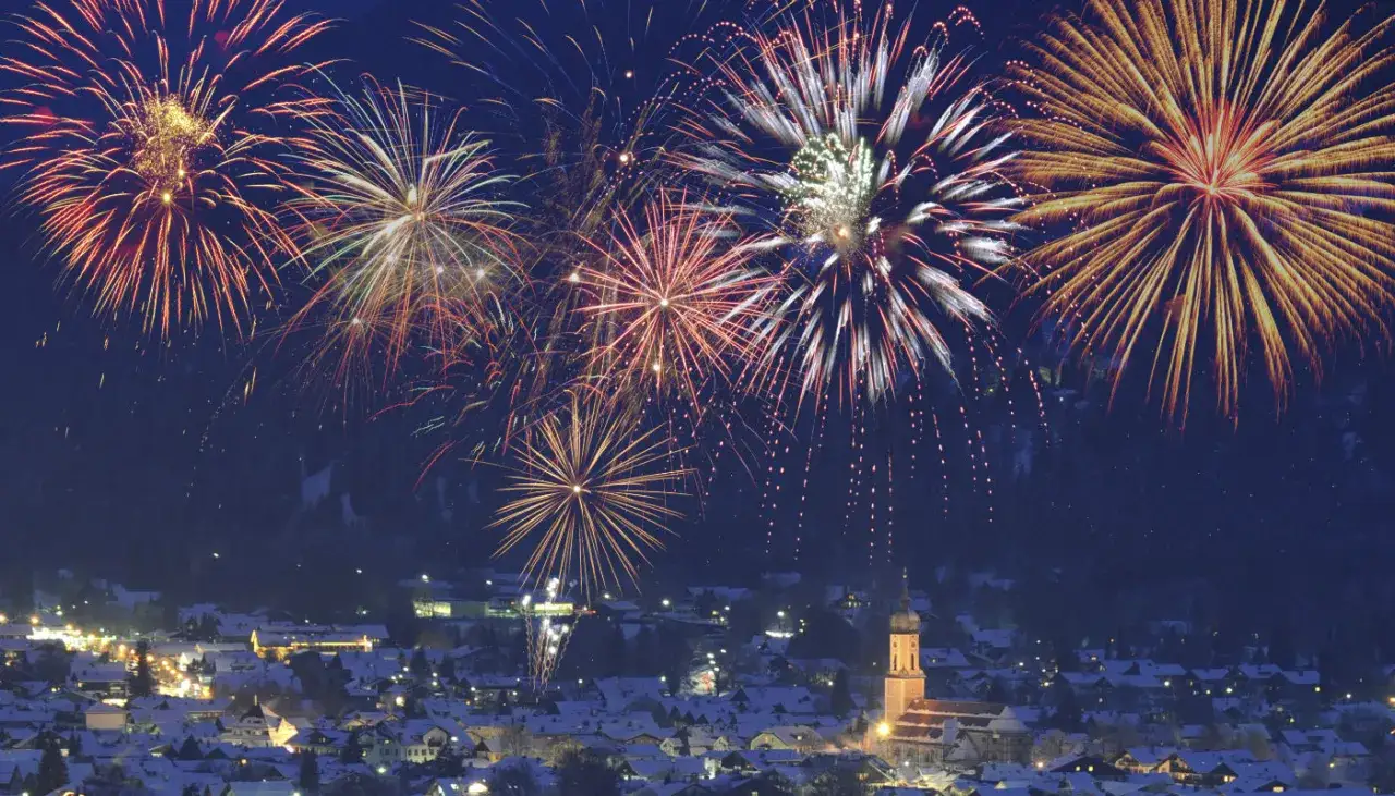 Feuerwerk erhellt den Nachthimmel über einem verschneiten Dorf in Deutschland. Ein Fest für die Sinne zum Jahreswechsel.