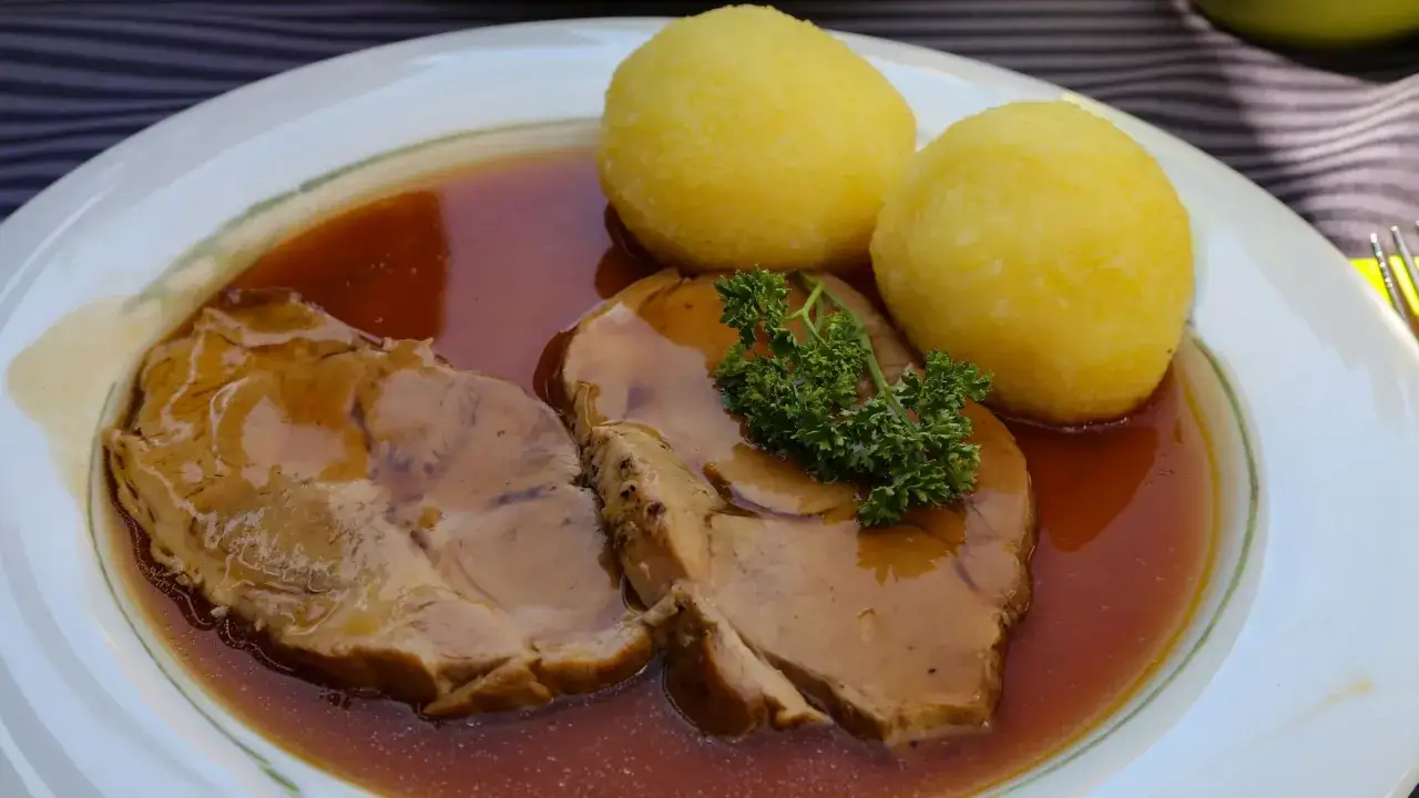 Zarte Scheiben Sauerbraten mit zwei Klößen und kräftiger Soße, garniert mit Petersilie. Ein klassisches Sauerbraten Rezept, das man probieren muss!