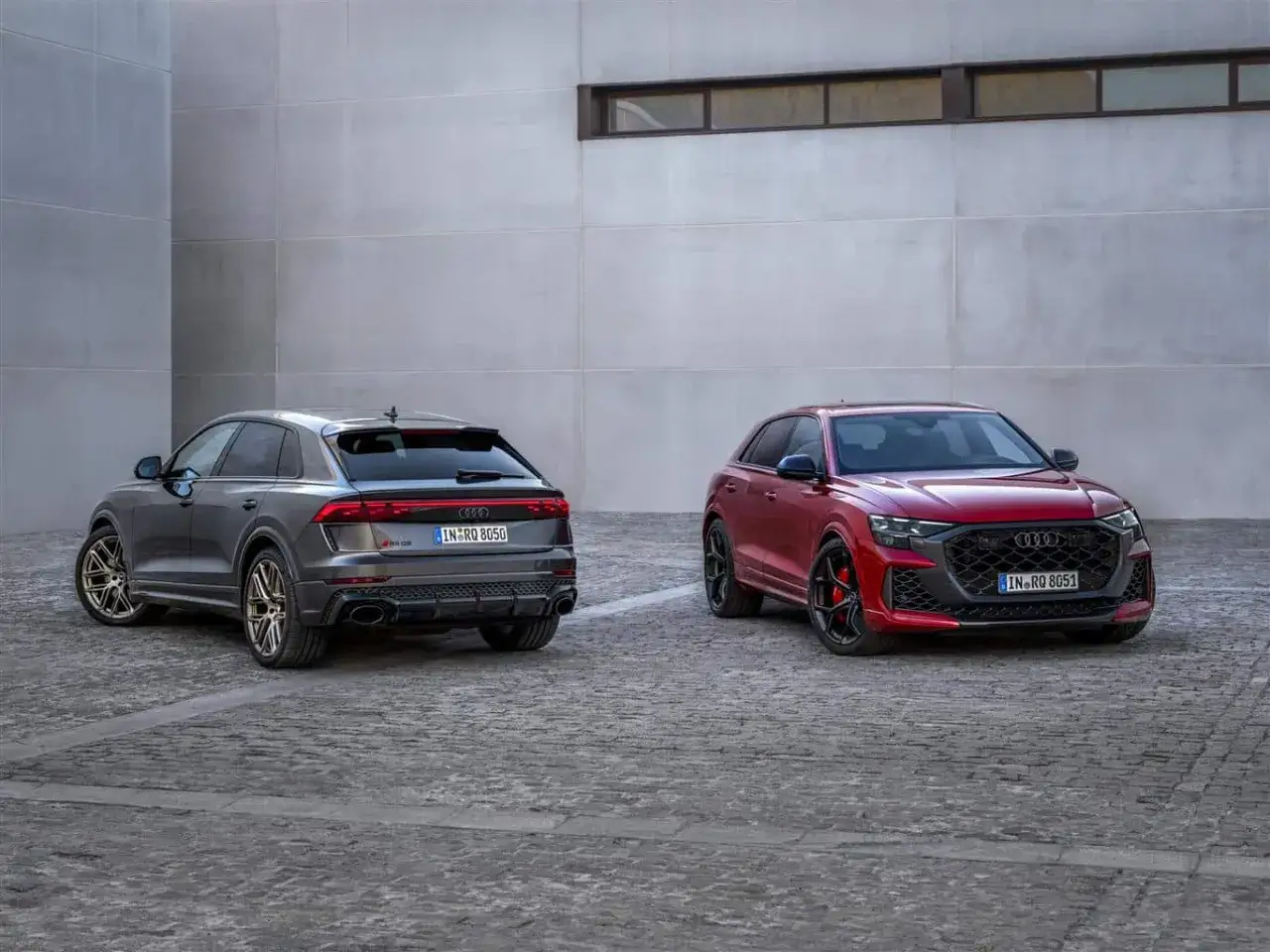 Due Audi RS Q8, una grigia e una rossa, parcheggiate su un selciato di fronte a un edificio moderno.