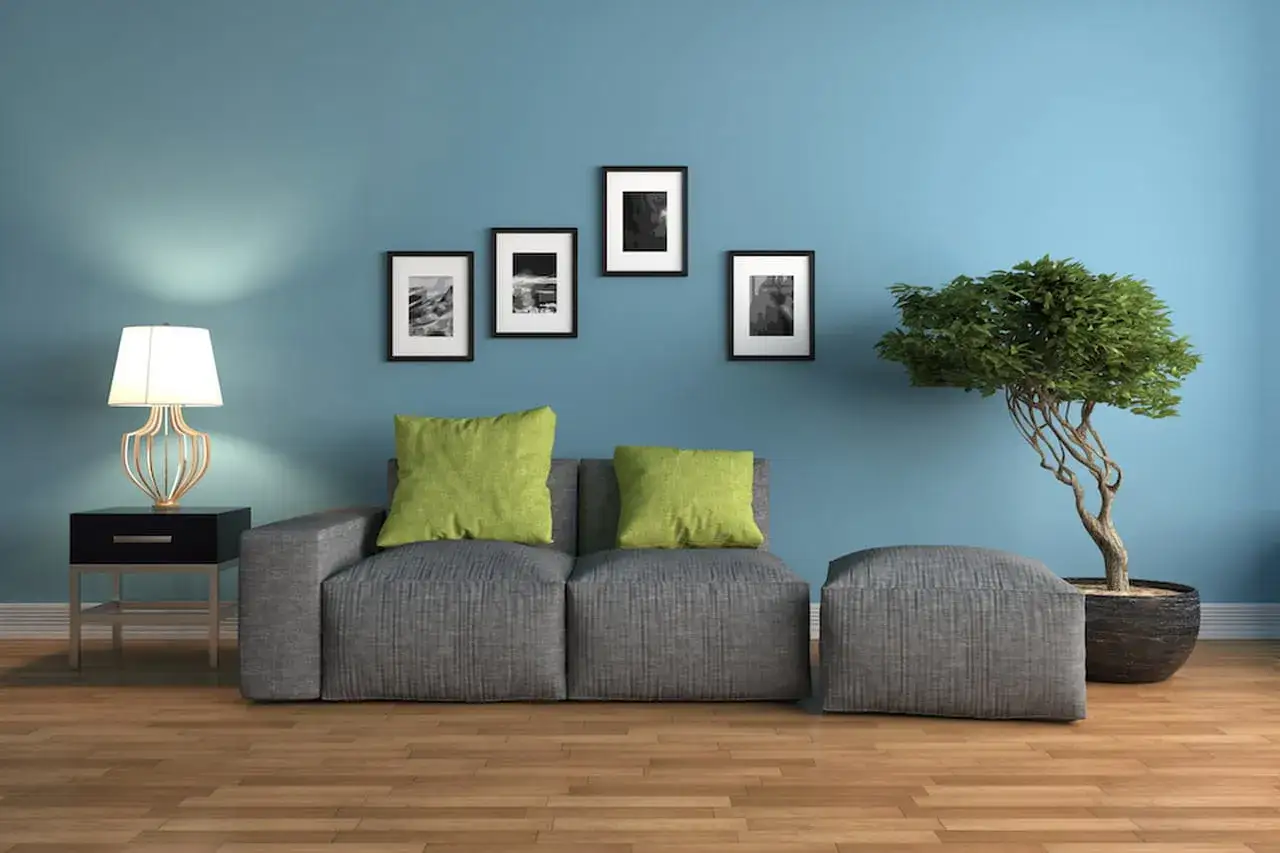 Soggiorno con divano grigio, cuscini verdi, quadri astratti e un bonsai su sfondo blu con **colori freddi**.