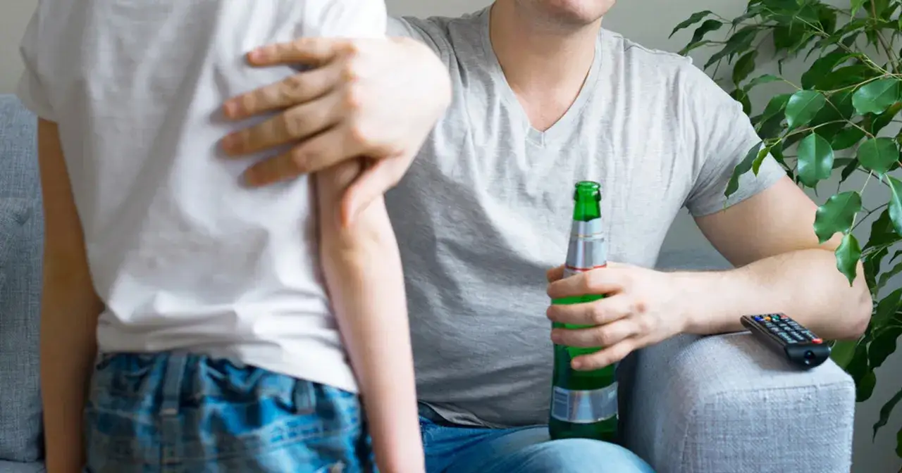 Ojciec z piwem w ręku pociesza dziecko. Pijane dziecko konsekwencje dla rodziców mogą być poważne.