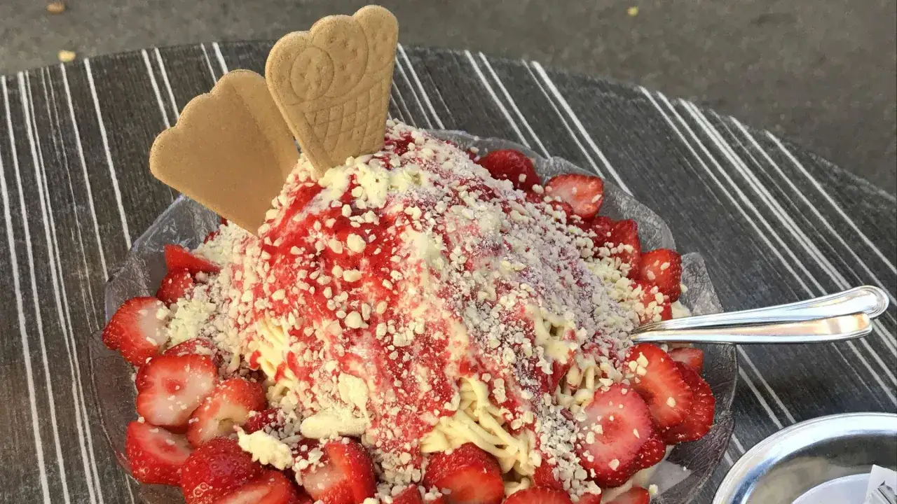 Ein köstliches Spaghetti-Eis-Dessert mit frischen Erdbeeren, Erdbeersauce und weißen Schokostückchen, garniert mit zwei Waffeln.