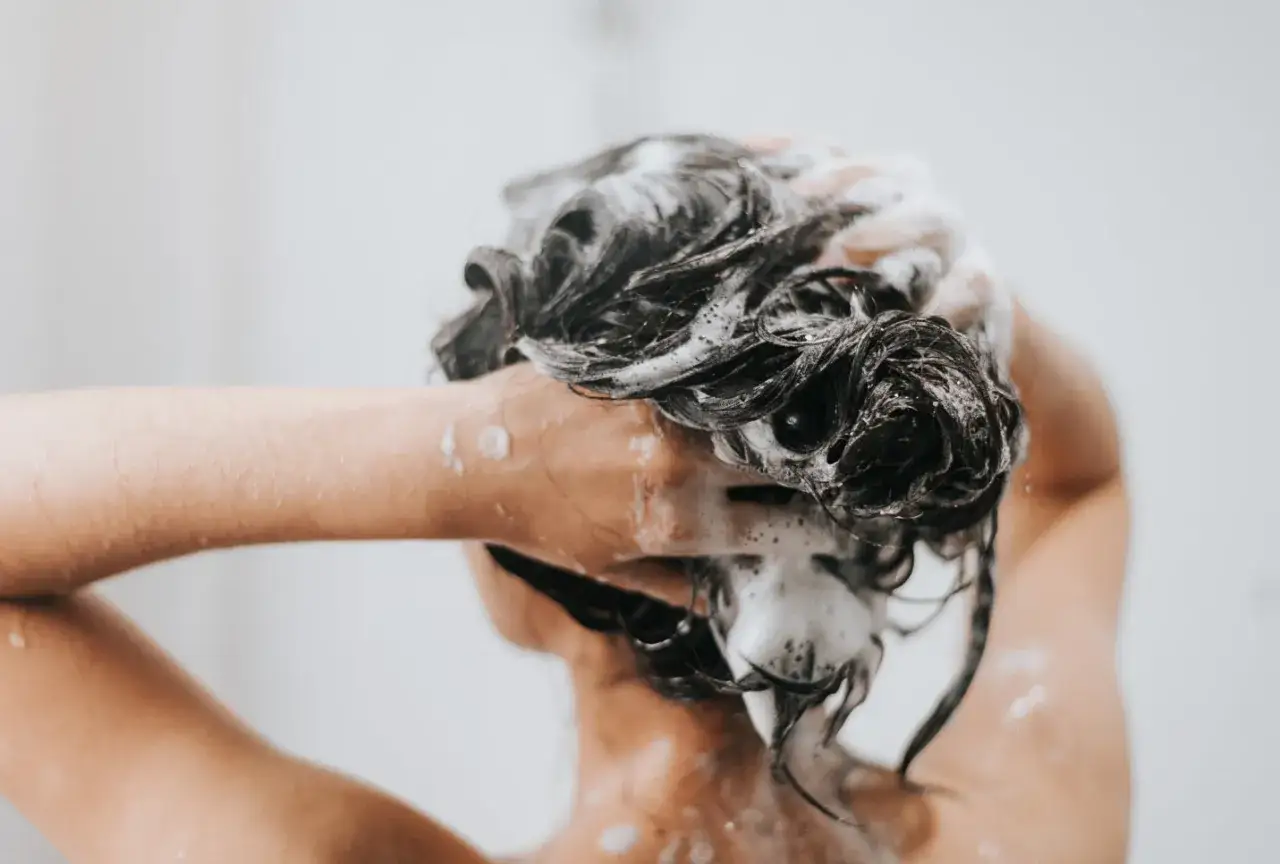 Schaumige Haare werden von einer Hand gewaschen. Die Frage: conditioner vor oder nach shampoo?