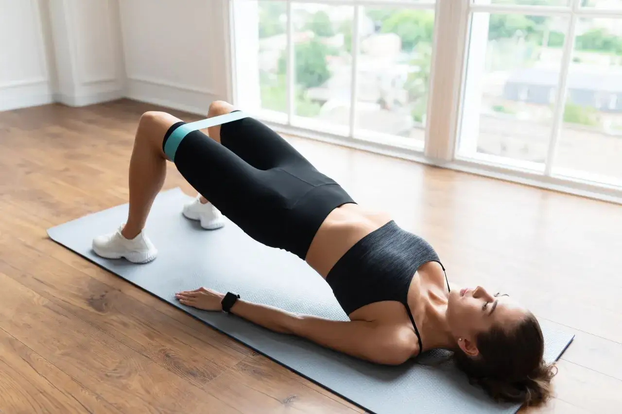 Femme effectuant un exercice culotte de cheval avec un élastique pour renforcer ses fessiers.