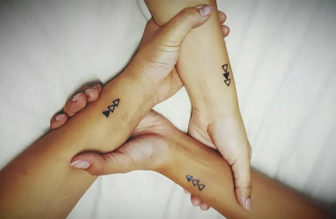 Tre handleder med matchande tatueringar av tre trianglar som symboliserar tatuering systerskap.