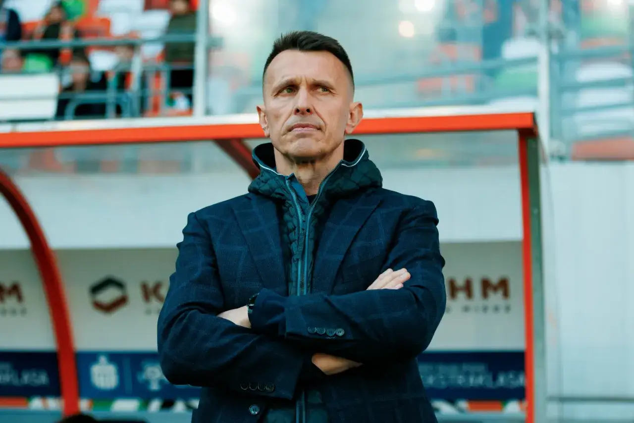Trener Zagłębia Lubin z założonymi rękami, w garniturze i kamizelce, patrzy w dal.