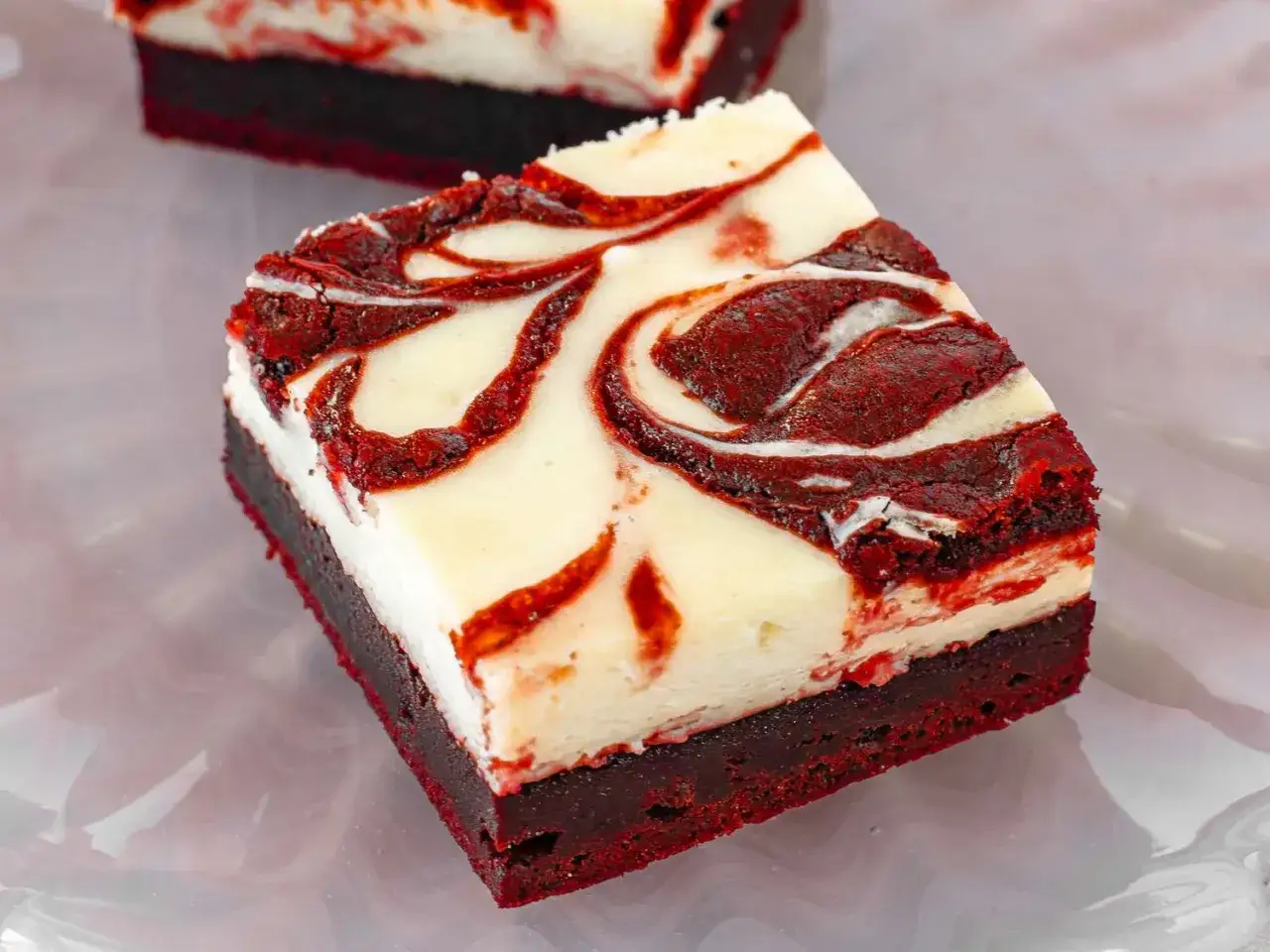 Zwei Stücke Red Velvet Cheesecake Brownies mit wirbelnder Käsekuchenschicht auf einem dunklen Brownie-Boden.
