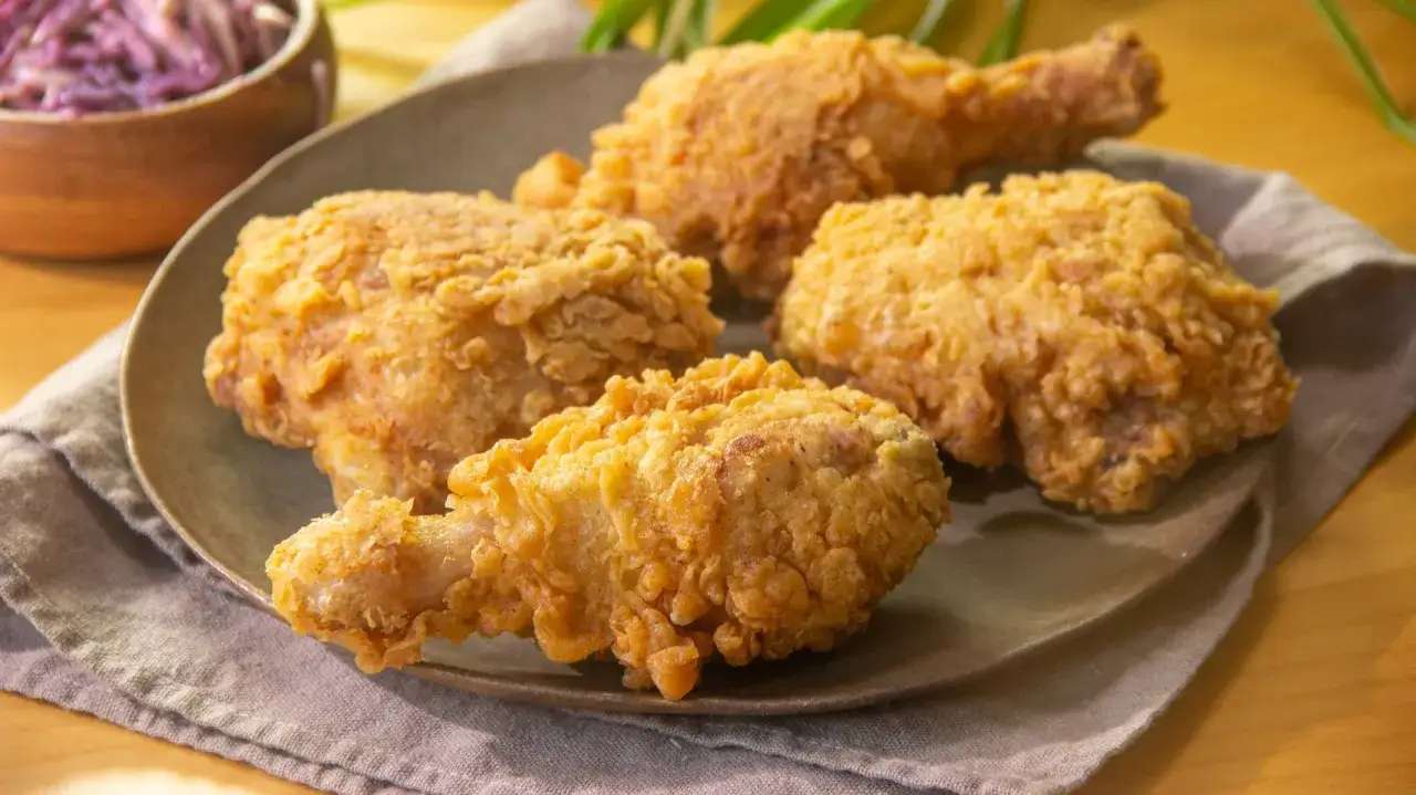 Cuatro piezas de crujiente pollo frito doradas y apetitosas, servidas en un plato con una ensalada morada al fondo.