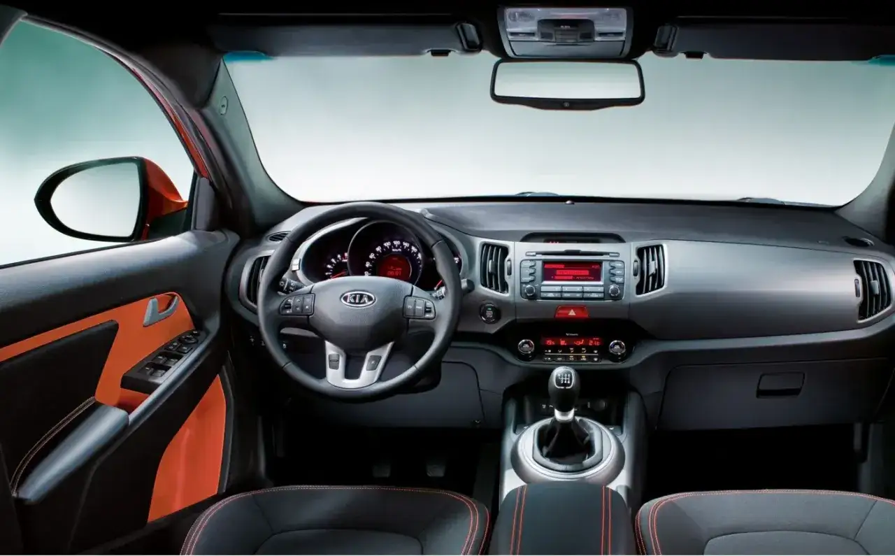 Wnętrze Kia Sportage 2014 z pomarańczowymi akcentami na drzwiach i siedzeniach. Widoczna kierownica, deska rozdzielcza i konsola środkowa.
