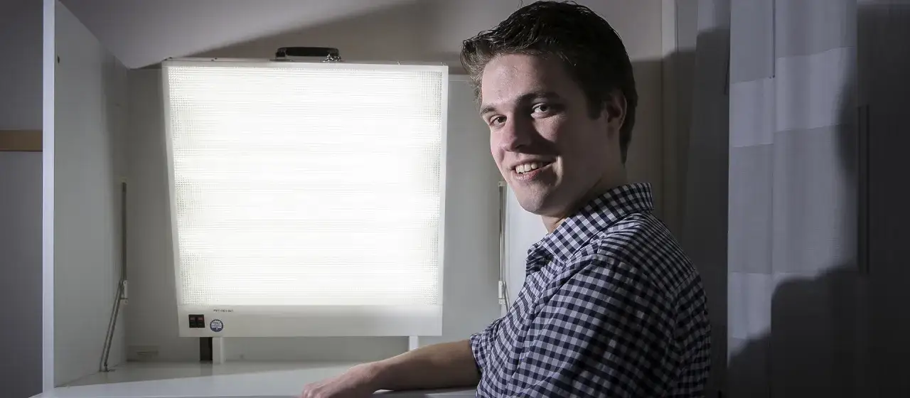 Jonge man lacht naar camera, naast een lichttherapie lamp, een van de 6 alternatieven voor antidepressiva.