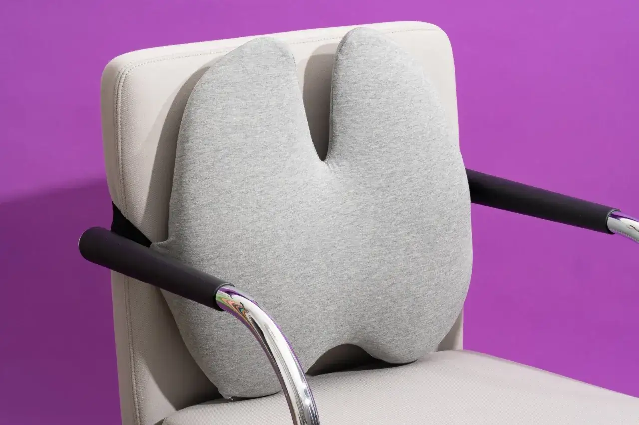 A grey almohada lumbar is attached to a light-colored chair, offering ergonomic support.