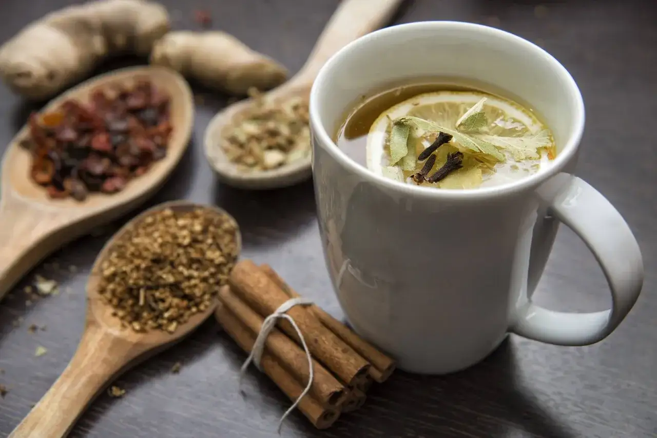 Zutaten f&uuml;r **chai selber machen**: Ingwer, Zimt, Gew&uuml;rze auf L&ouml;ffeln und eine Tasse mit Tee, Zitrone und Kr&auml;utern.