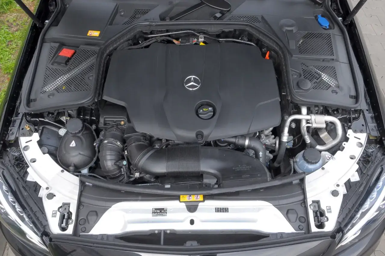 Silnik w Mercedes-Benz Klasa C. Czarna osłona z logo producenta, widoczne przewody i elementy układu dolotowego.
