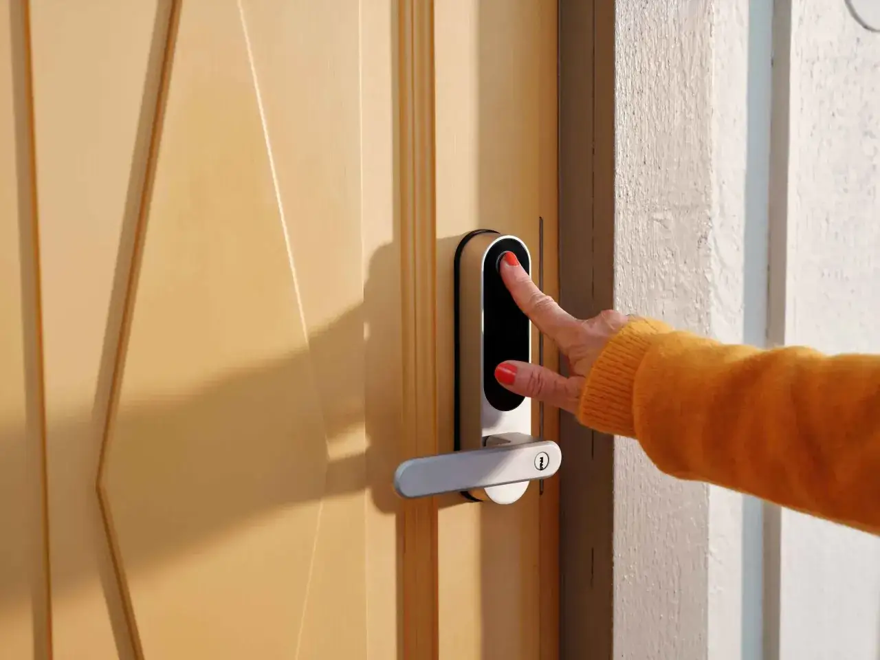 En hand med orange tr&ouml;ja och r&ouml;da naglar testar fingeravtrycksl&auml;saren p&aring; ett Nimly Touch Pro d&ouml;rrl&aring;s.