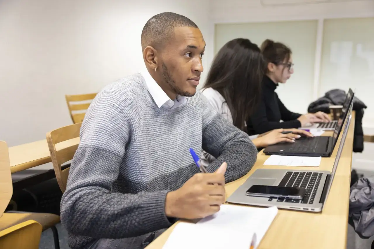 Des étudiants suivent des programmes MBA en ligne, concentrés sur leurs ordinateurs portables dans une salle de classe.