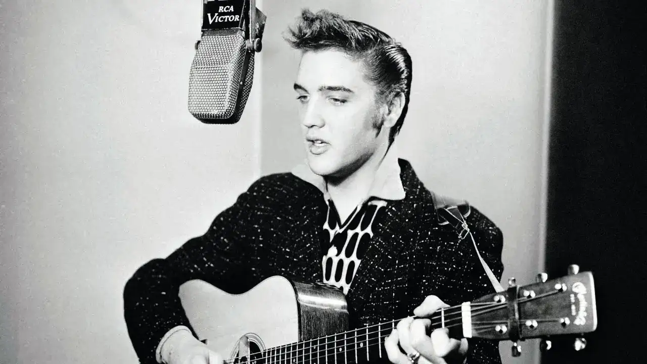 Junger Elvis Presley spielt Gitarre vor einem RCA Victor Mikrofon.