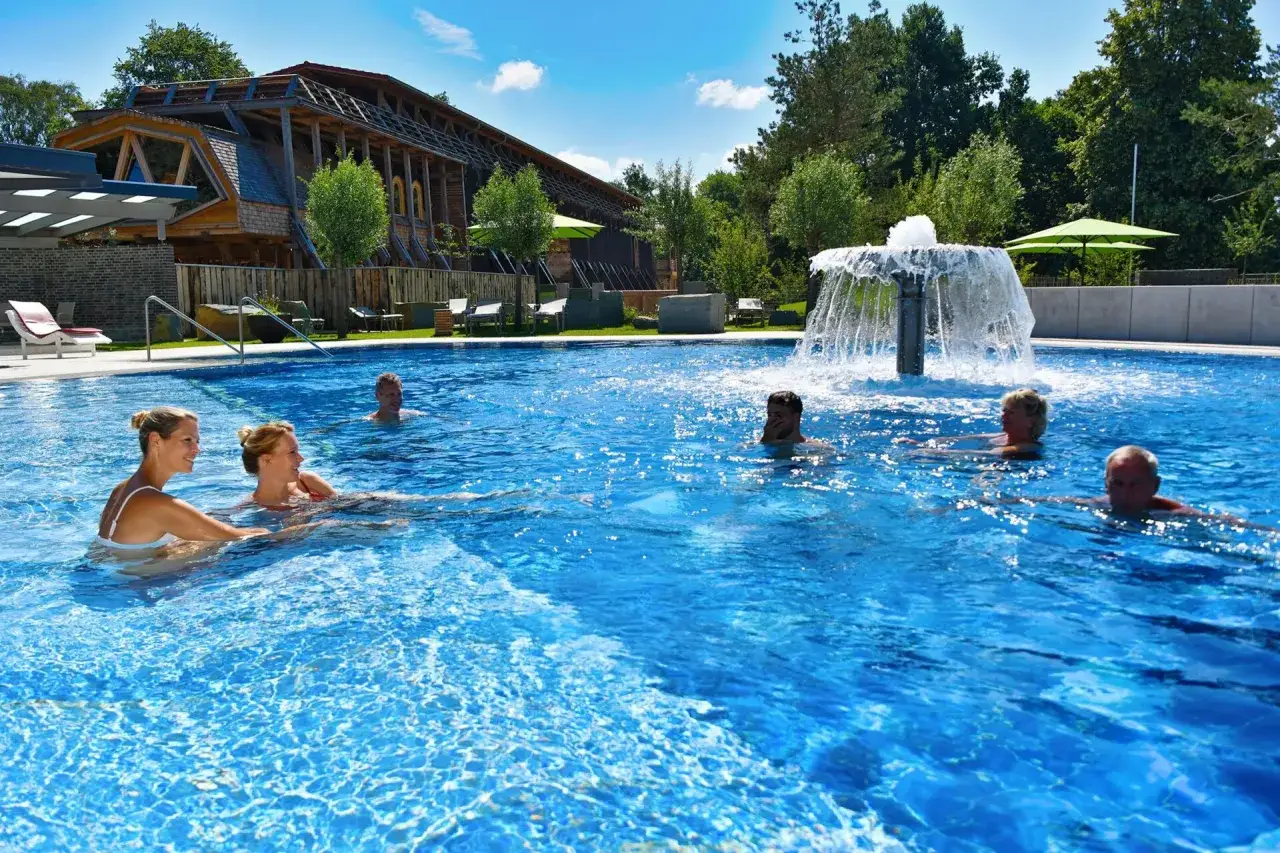 Entspannte Menschen genießen das Schwimmbad eines Kurortes in NRW. Ein Brunnen sprudelt im Hintergrund.