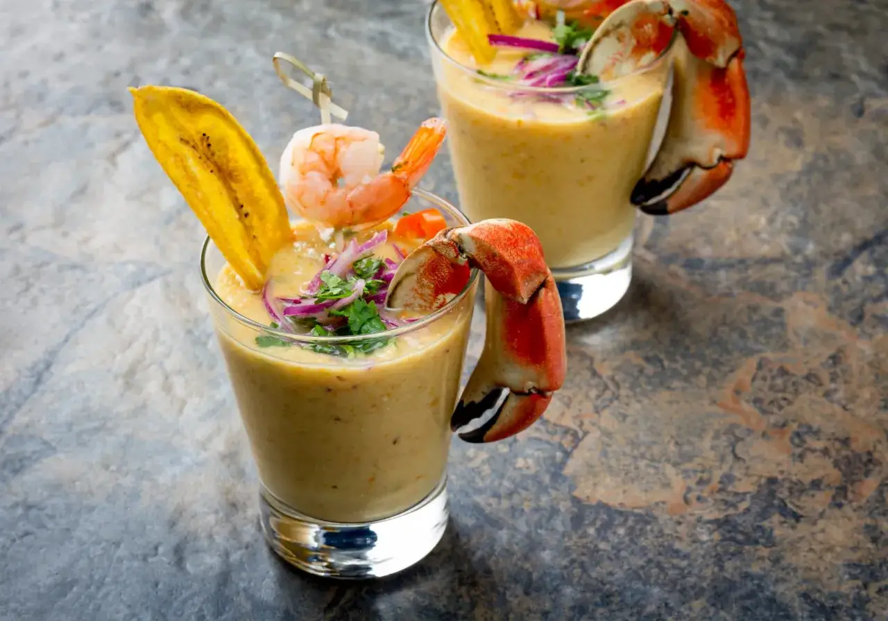 Zwei Gl&auml;ser mit cremiger Tigermilch, garniert mit Garnelen, Bananenchips und Krabbenkrallen.