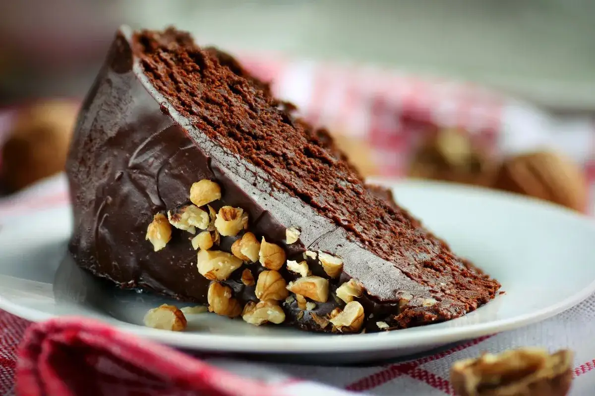 Ein saftiges Stück schoko nuss kuchen mit glänzender Schokoladenglasur und gehackten Nüssen, serviert auf einem weißen Teller.