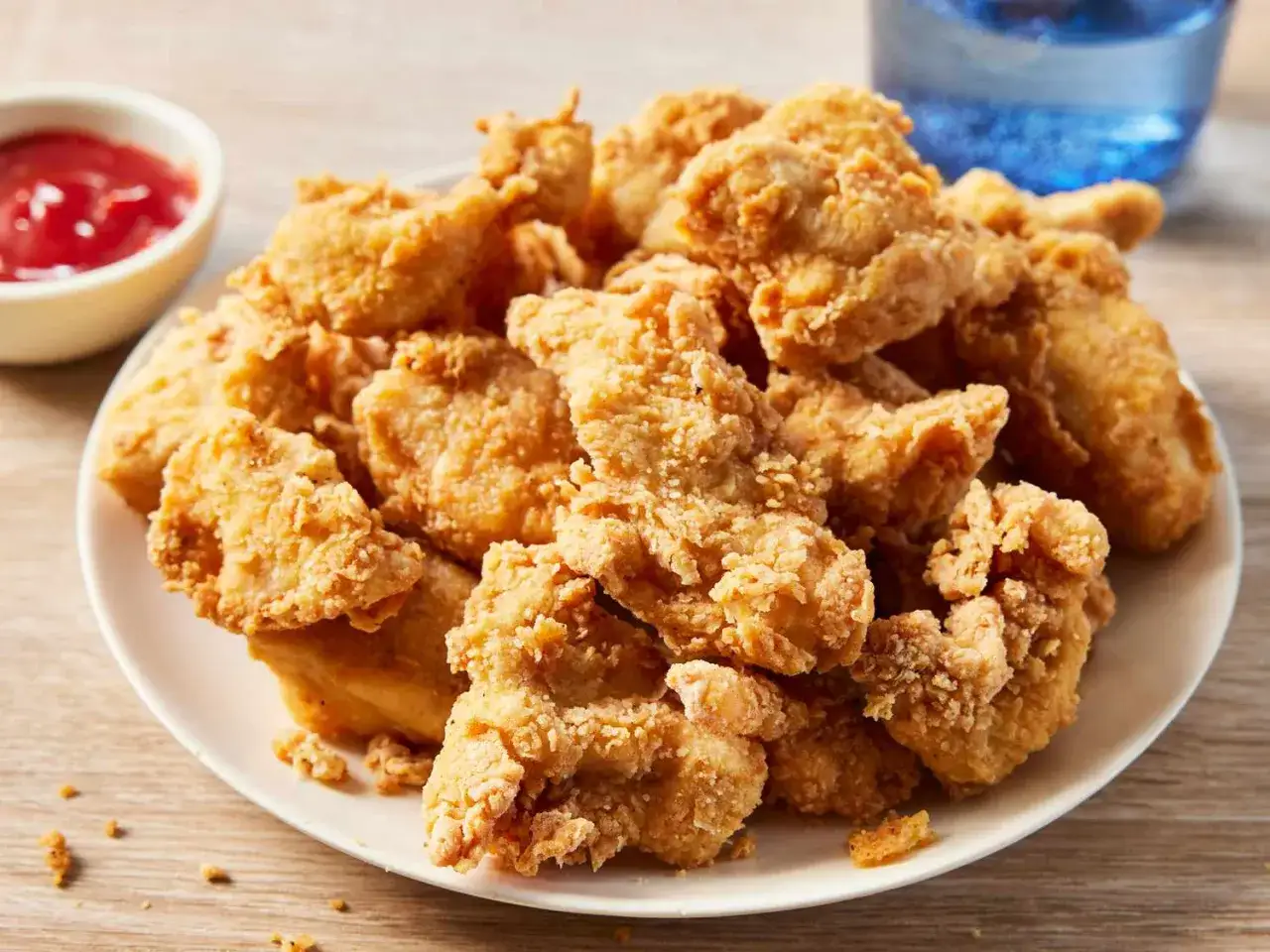 En tallrik med gyllene, krispiga chicken nuggets. En liten sk&aring;l med ketchup och ett glas vatten i bakgrunden.