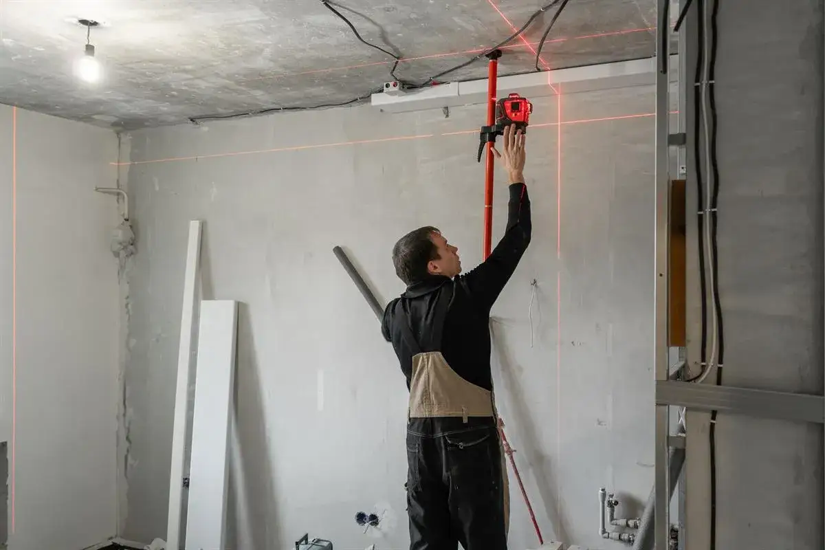 Budowlaniec ustawia laser, który wyznacza idealne **piony** i poziomy na ścianach.