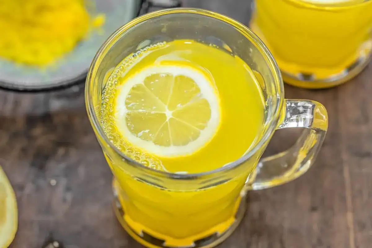 Ein Glas mit leuchtend gelbem Ingwer Zitrone Tee selber machen ist einfach. Eine Zitronenscheibe schwimmt obenauf.