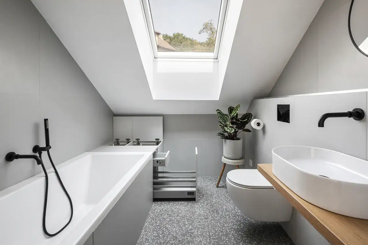 Piccolo bagno sottotetto basso con vasca, lavabo, WC e lucernario.