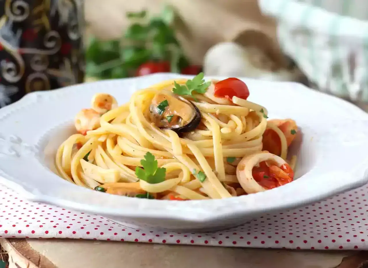 Un piatto invitante di pasta con pesce, cozze, gamberi e calamari, condito con pomodorini e prezzemolo fresco.