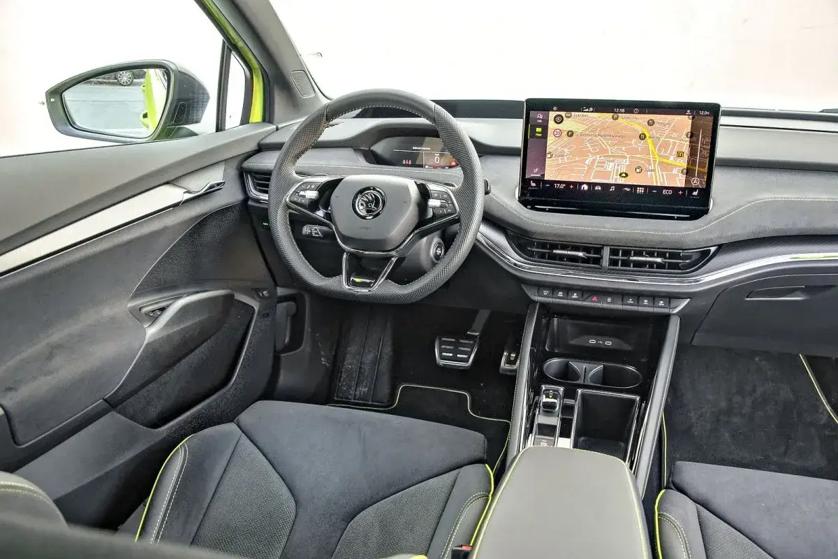 Wnętrze Skoda Enyaq Coupe: kierownica, duży ekran multimedialny z nawigacją, fotele z żółtymi akcentami.