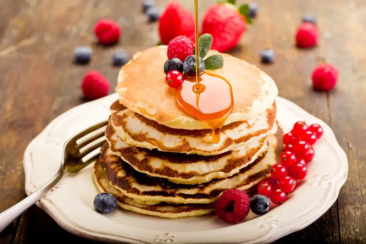 Pila di pancake soffici, guarniti con frutti di bosco e sciroppo d'acero. Perfetti per una ricetta pancake veloce senza lievito.