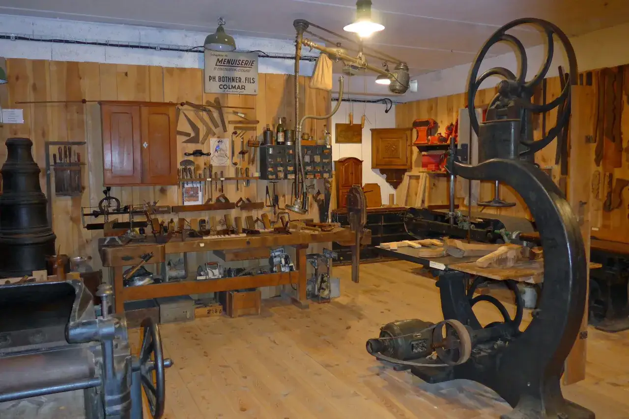 Atelier de menuiserie avec établi, outils anciens et une machine à faire de la sciure de bois.