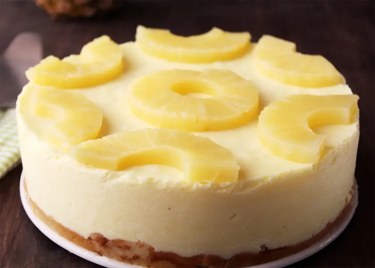 Tarta de piña cremosa, decorada con rodajas y trozos de piña fresca. Un postre tropical irresistible.