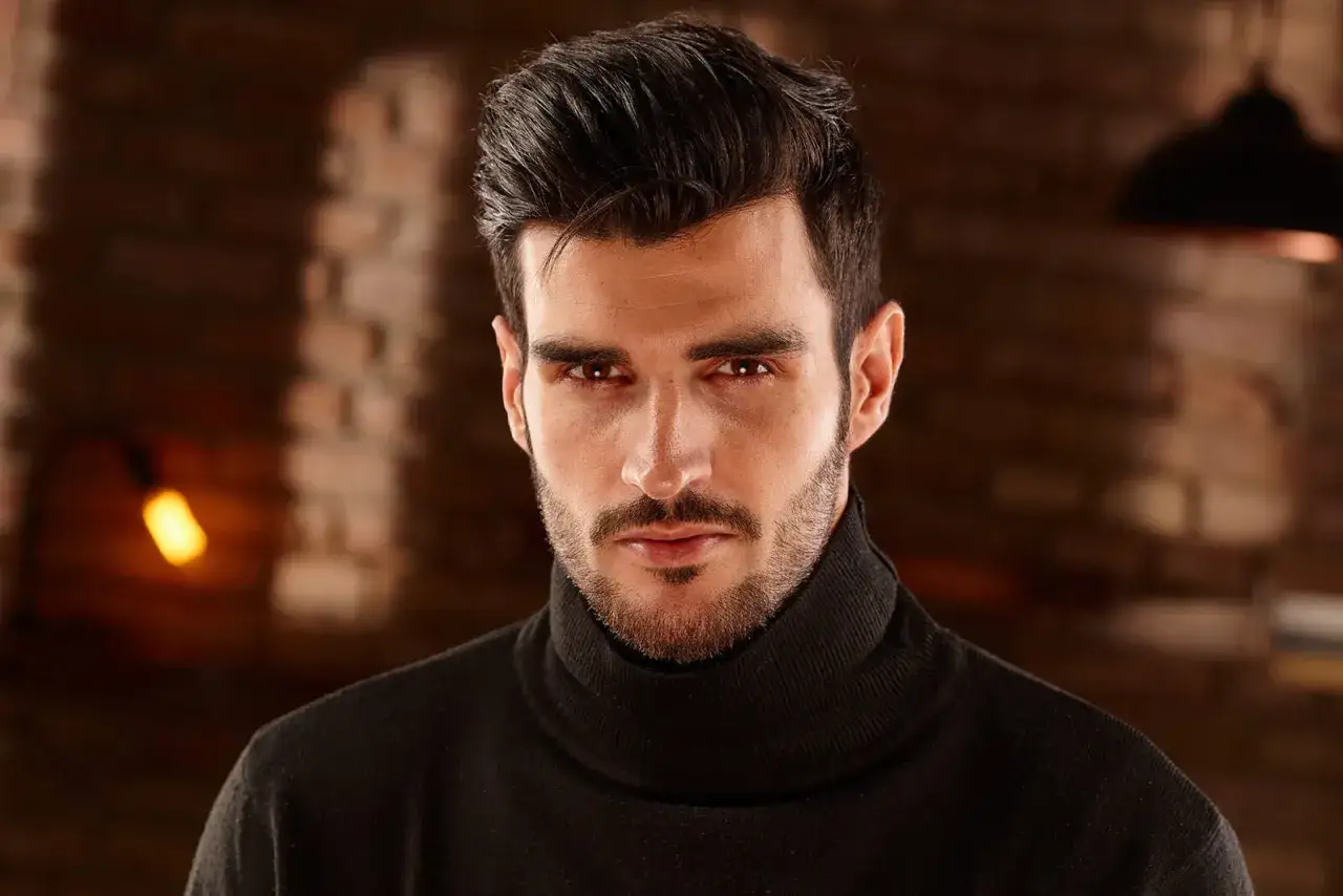 Un homme au regard intense, portant un col roulé noir. Sa barbe de 3 jours, d'environ 3 mm, complète son allure.