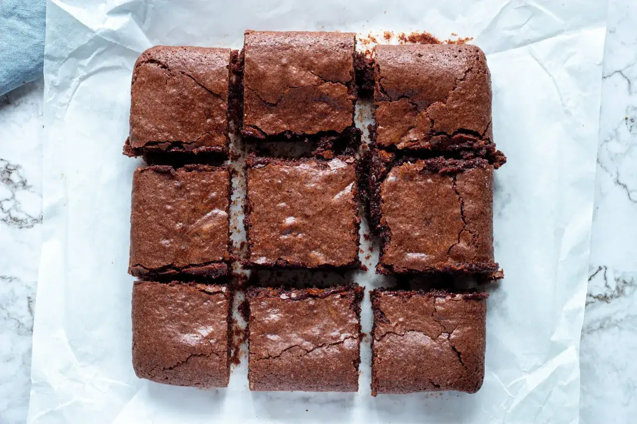 Nio bitar saftig, glutenfri brownie ligger upplagda p&aring; bakpl&aring;tspapper. Perfekt f&ouml;r fikat!