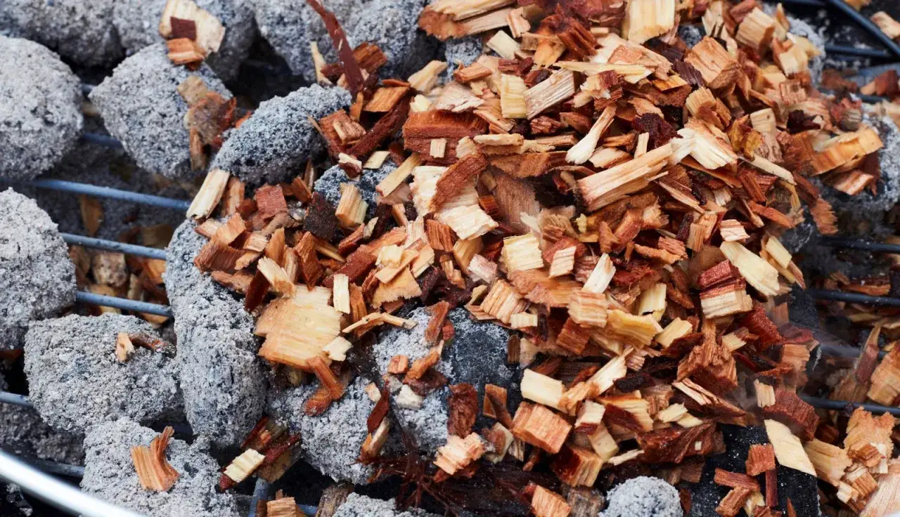 Des copeaux de bois sur des braises grises, prêts pour le fumage barbecue gaz. L'arôme promet un délice.