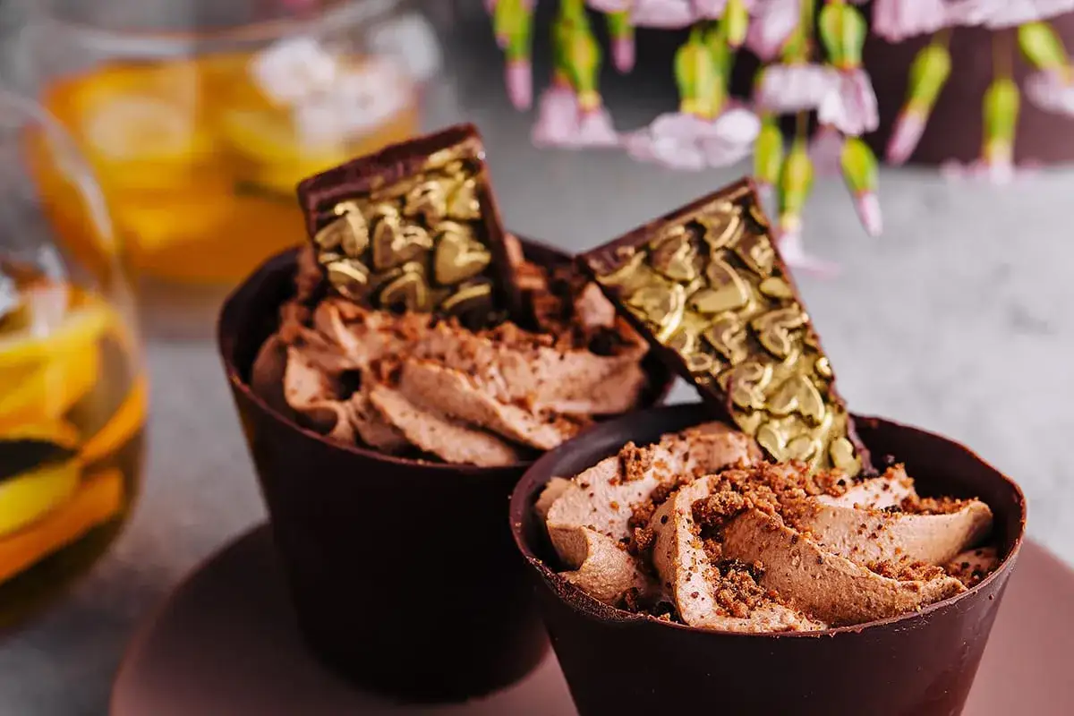Deux coupelles de recette mousse au chocolat à l'ancienne, garnies de copeaux dorés en forme de cœur.