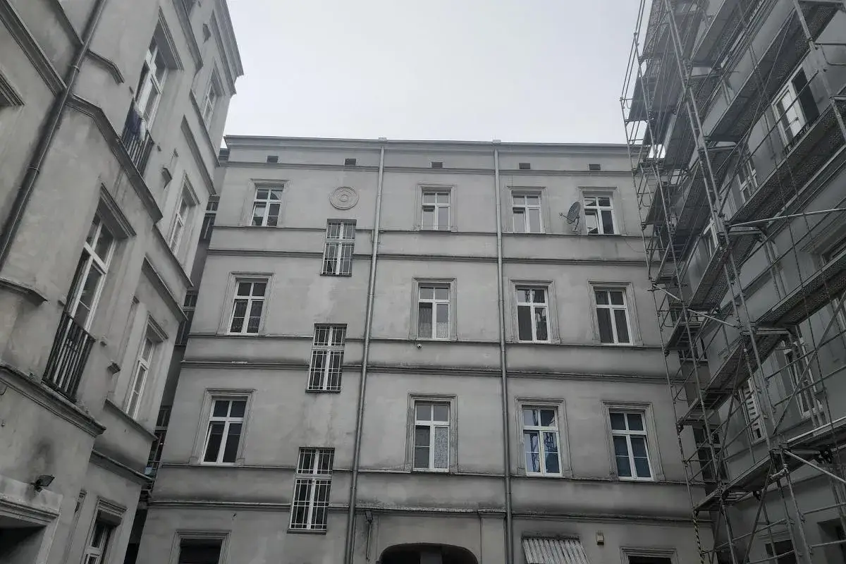 Oficyna co to? Szare kamienice z oknami, jedna z nich w rusztowaniach.