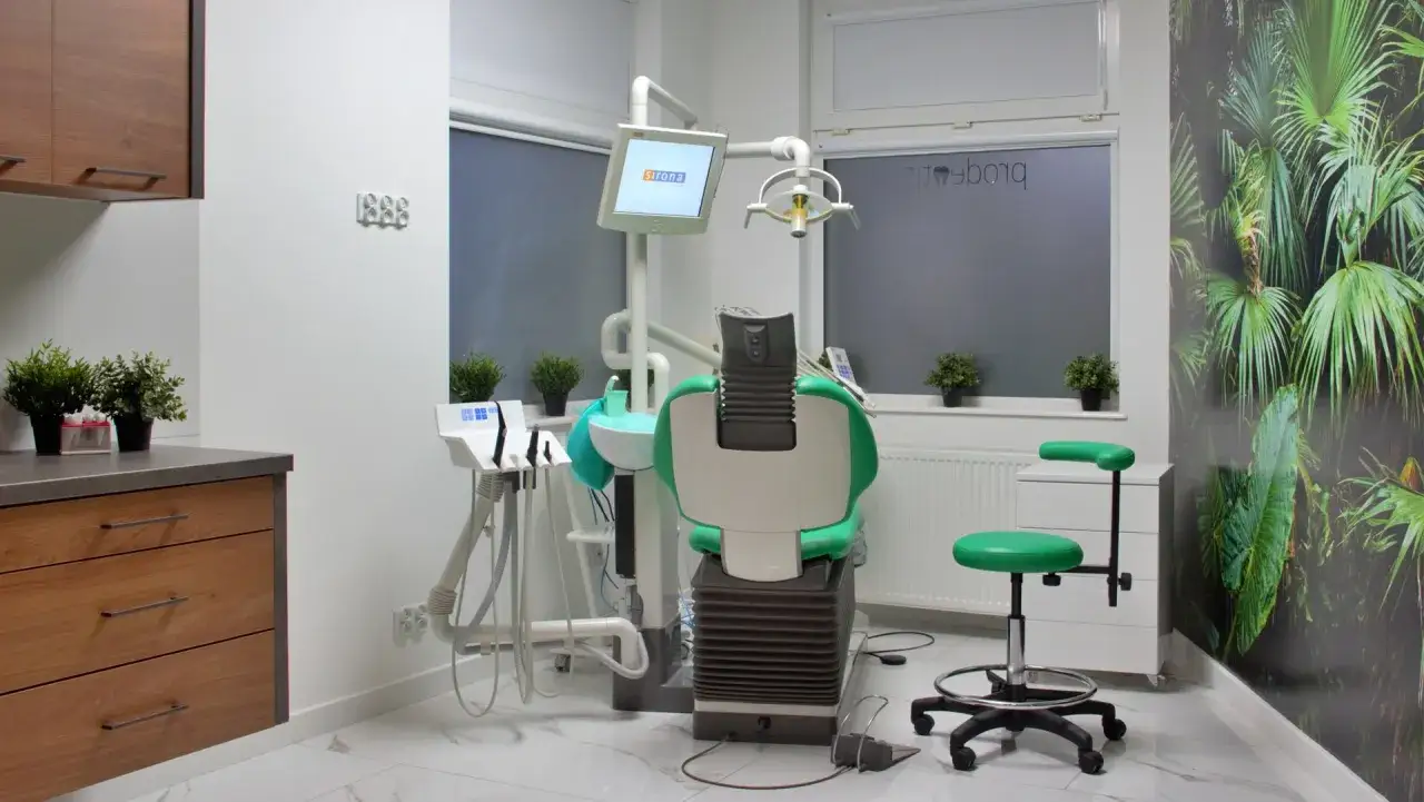 Nowoczesny gabinet stomatologiczny z zielonym fotelem, monitorem Sirona i tapetą z motywem roślinnym.