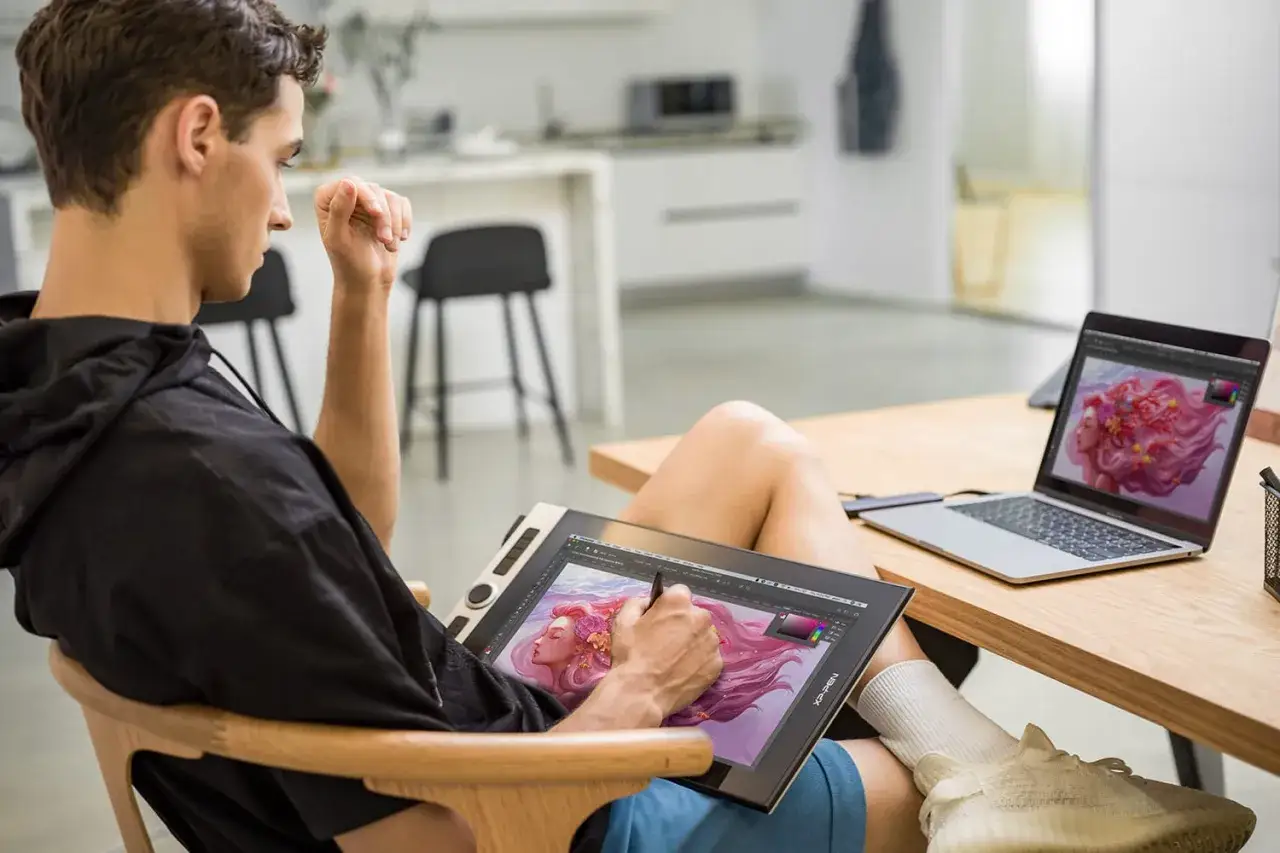 Un jeune homme utilise une tablette graphique et un ordinateur portable pour sa **configuration PC graphiste**. Il dessine une sirène aux cheveux roses.
