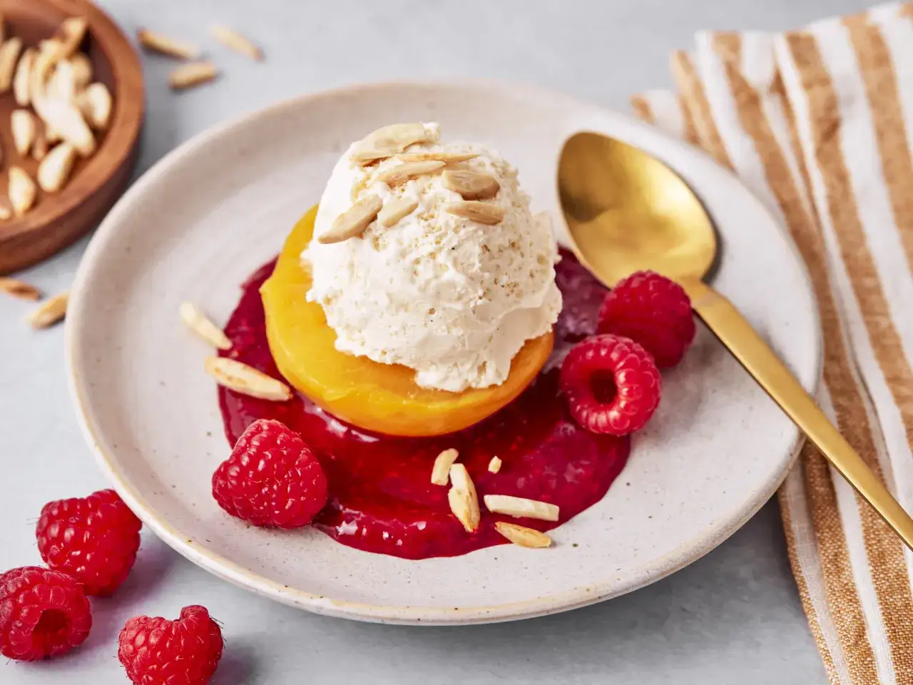 Ein Pfirsich Melba Dessert mit einer Kugel Vanilleeis, Himbeersauce, frischen Himbeeren und Mandelbl&auml;ttchen.