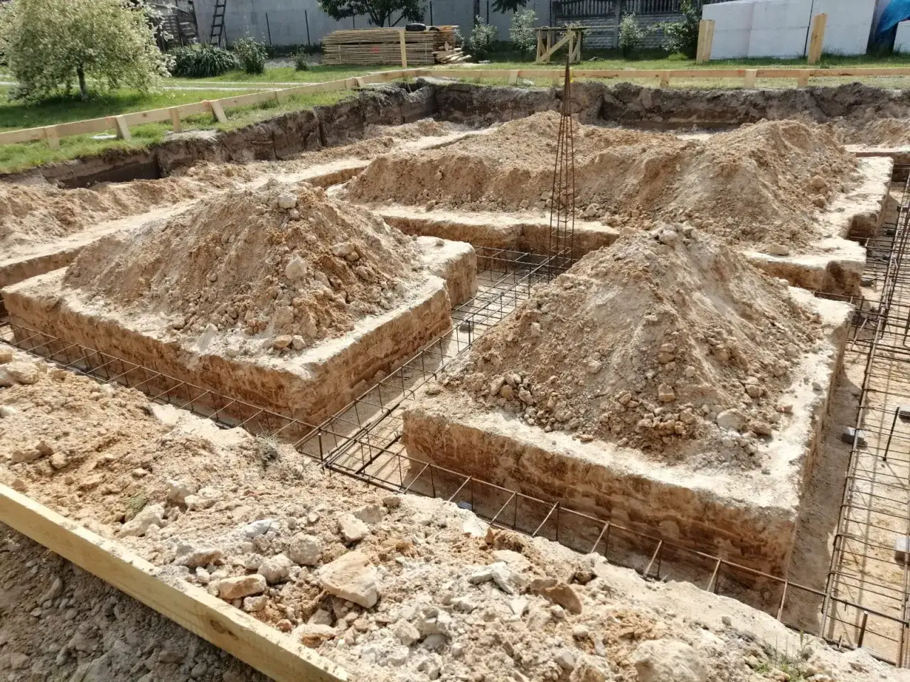 Wykop pod fundamenty bez szalunku, z widoczną zbrojeniem i usypaną ziemią.
