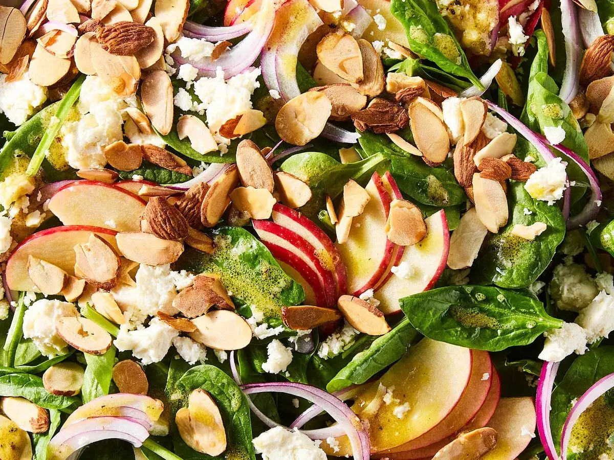 Ensalada de espinacas con trozos de manzana roja, almendras tostadas, queso blanco desmoronado y cebolla morada.