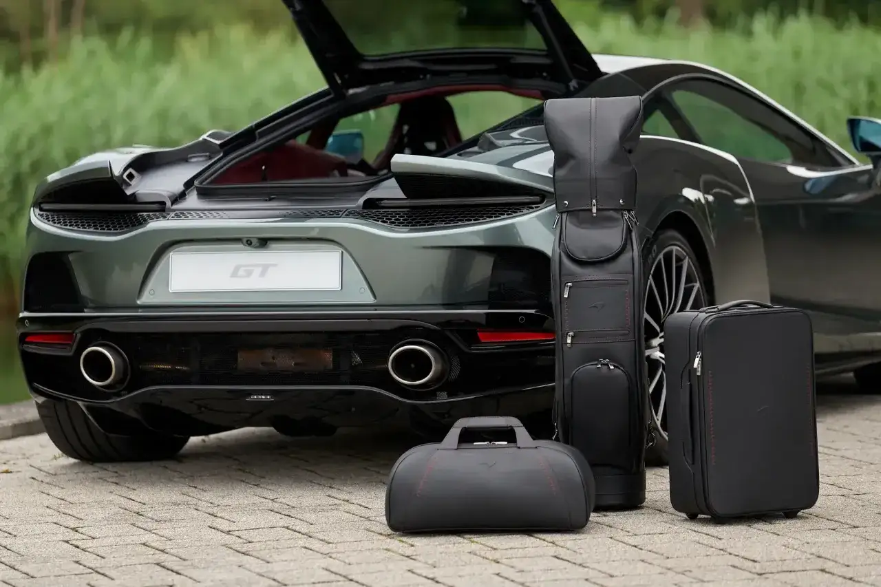 Zielony McLaren GT z otwartą klapą bagażnika i kompletem czarnych, skórzanych toreb podróżnych.