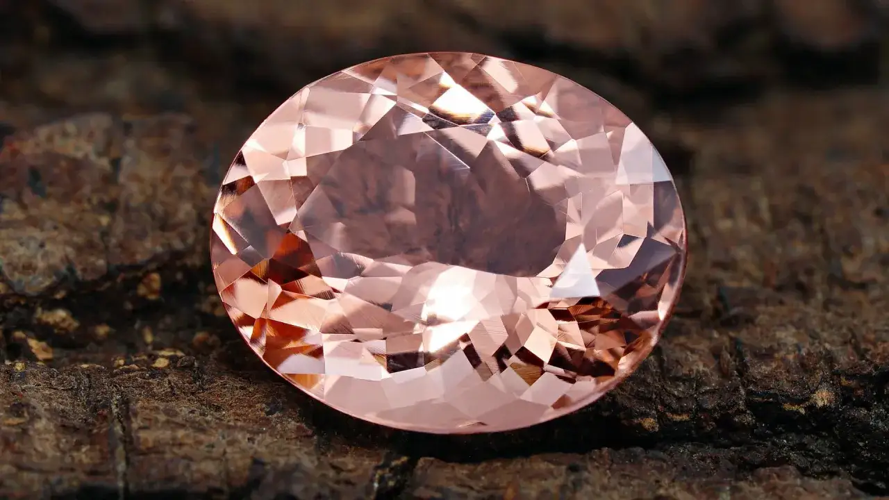 En stor, fasetterad morganit ädelsten med rosa nyanser, som vilar på en grov, mörk yta. Dess morganit egenskaper lyser i ljuset.