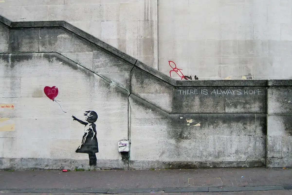 Dziewczynka puszcza czerwony balon w kształcie serca. To dzieło Banksy'ego, kt&oacute;ry pyta kim jest. Napis 