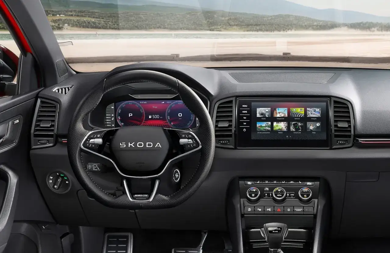 Wnętrze Skoda Karoq Sportline z cyfrowymi zegarami i ekranem multimediów. Widok na plażę przez przednią szybę.