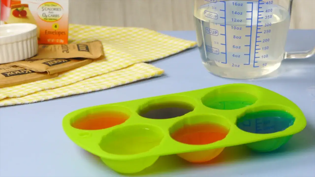 Préparation de gelatine en poudre comment l'utiliser : des sachets Knox, un moule en silicone rempli de gelées colorées et un verre doseur.