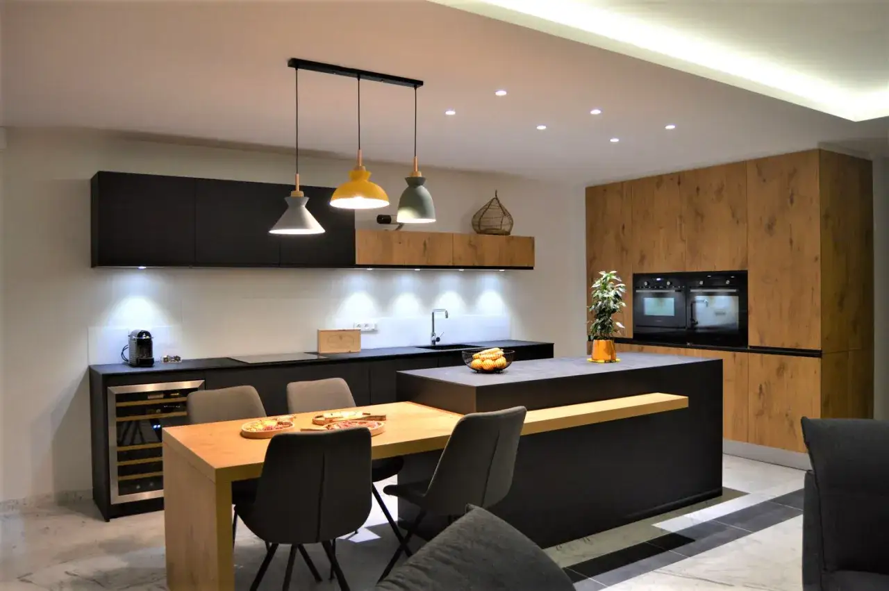 &Eacute;l&eacute;gante cuisine beige et noir avec &icirc;lot central, table en bois et chaises grises. L'espace est moderne et lumineux.