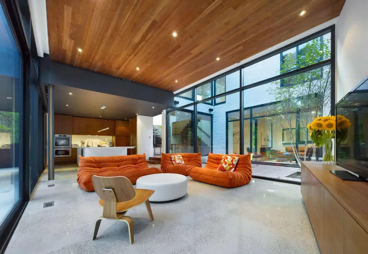 Modern living room in an architect's home in the ravine, featuring orange modular sofas, a wooden ceiling, and large windows overlooking a courtyard.