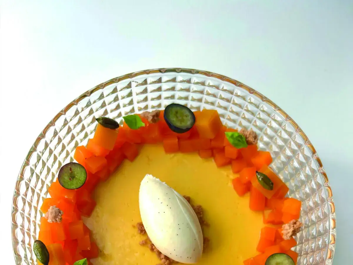 Delicioso flan de mango con helado de vainilla, trozos de mango fresco, ar&aacute;ndanos y hojas de menta en un plato de cristal.